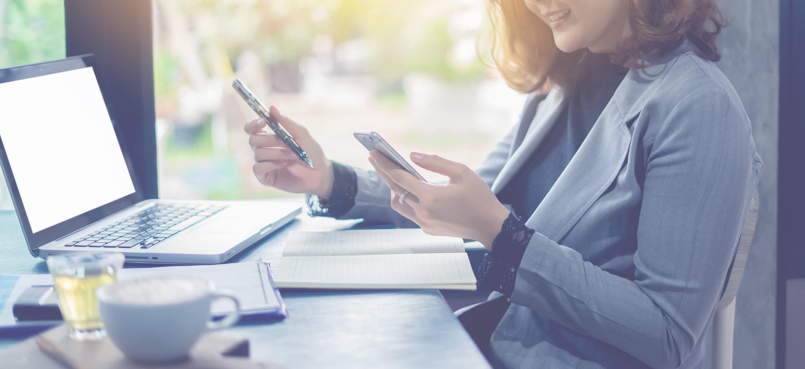 Woman at desk in front of laptop with mobile phone in hand